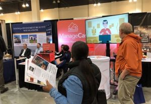 Trade show attendees engaging with the ManageCasa booth, viewing a product demo and collecting informational materials about the property management software.